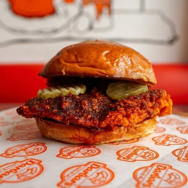 A crispy, spicy fried chicken sandwich with pickles on a brioche bun, on branded Dandan's paper.