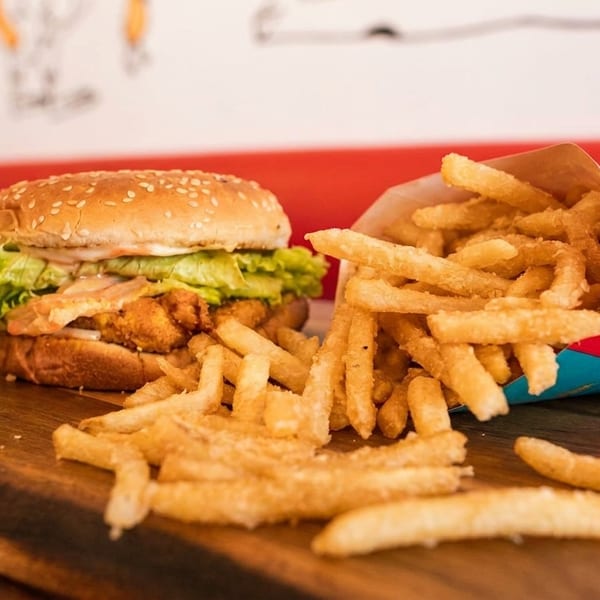 Crispy chicken burger with lettuce and sauce, alongside a carton of golden french fries on a wooden board.
