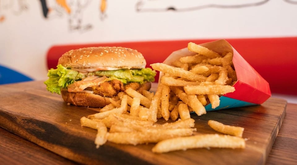 Crispy chicken burger with lettuce and sauce, alongside a carton of golden french fries on a wooden board.