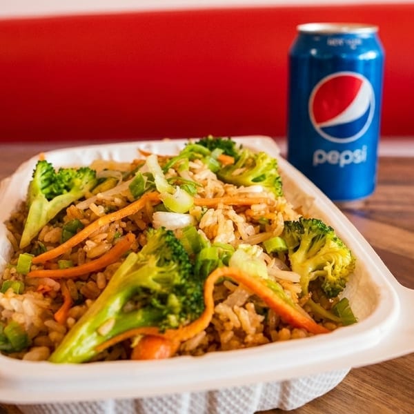Fried rice with broccoli, carrots, and scallions in a takeout container with a Pepsi can.