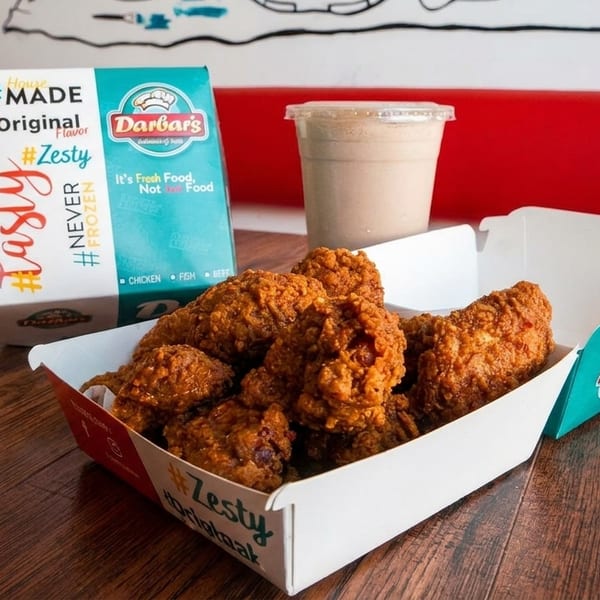 A box of crispy fried chicken pieces and a milkshake on a wooden table at Darbar's.