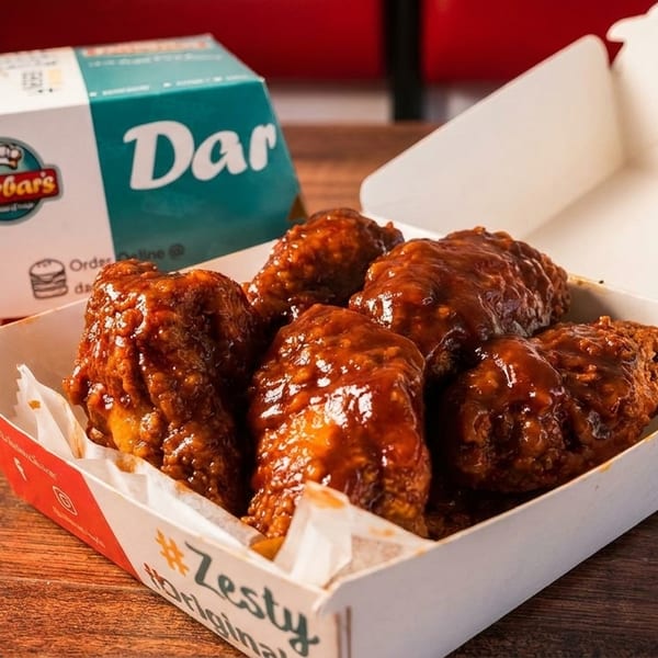 Darbar's Zesty Original chicken wings in a white and red takeout box on a wooden table.