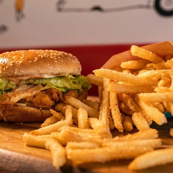 Crispy chicken burger with lettuce and sauce, alongside a carton of golden french fries on a wooden board.