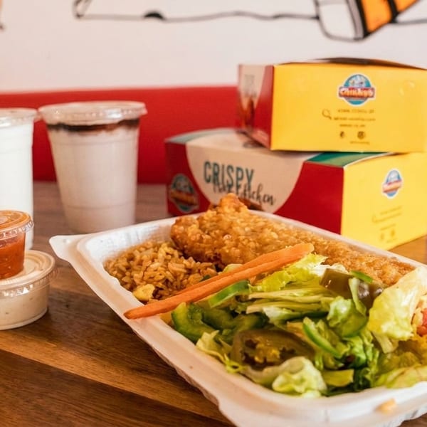Crispy chicken meal with rice, salad, sauces, and drinks on a wooden table.
