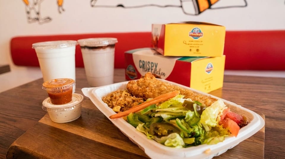 Crispy chicken meal with rice, salad, sauces, and drinks on a wooden table.