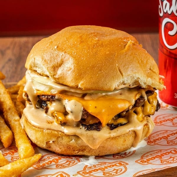 A double cheeseburger with melted cheese and sauce, fries, and a red Salaam Cola can.