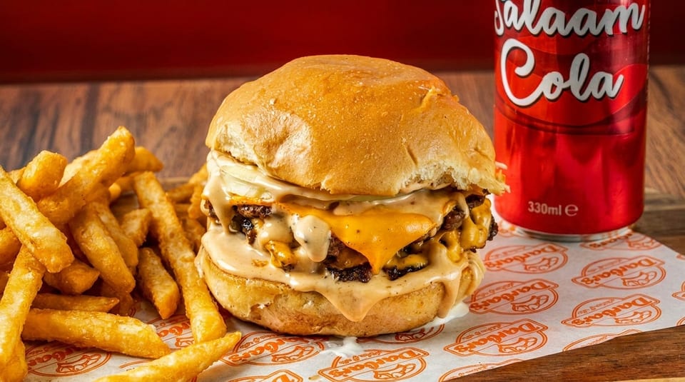 A double cheeseburger with melted cheese and sauce, fries, and a red Salaam Cola can.