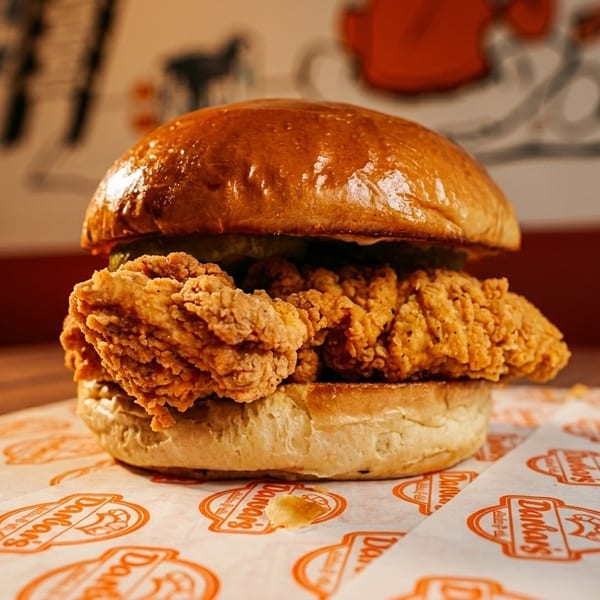 Crispy fried chicken sandwich with pickles on a brioche bun, on branded Dano's paper.