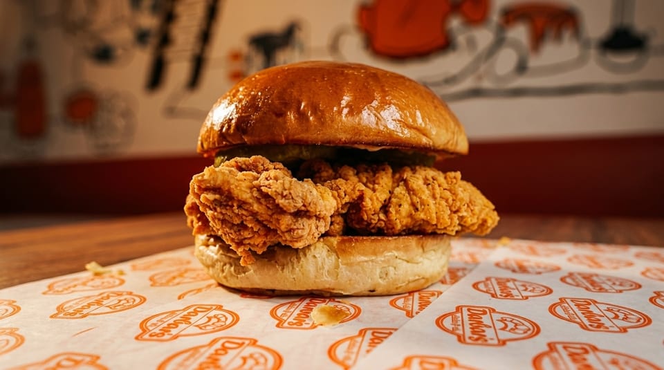 Crispy fried chicken sandwich with pickles on a brioche bun, on branded Dano's paper.